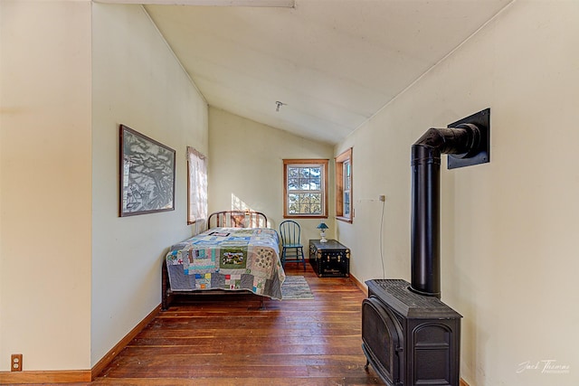 bedroom featuring lofted ceiling, a wood stove, wood-type flooring, and baseboards