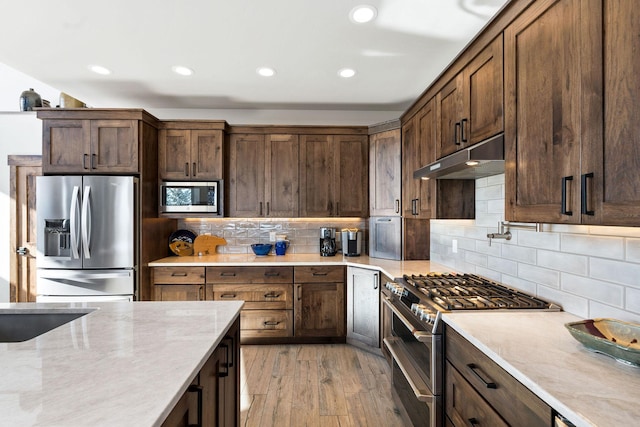 75 Meadows Dr, Whitefish, MT 59937 - kitchen featuring stainless steel appliances, under cabinet range hood, light stone countertops, light wood-style floors, and decorative backsplash