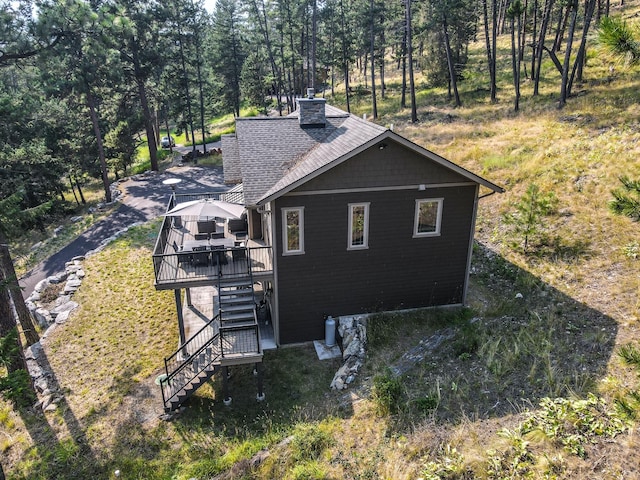 view of side of home with stairs, a deck, a chimney, and a shingled roof