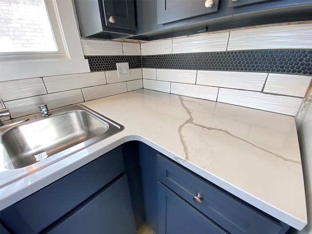 kitchen with a sink, blue cabinetry, backsplash, and light stone countertops