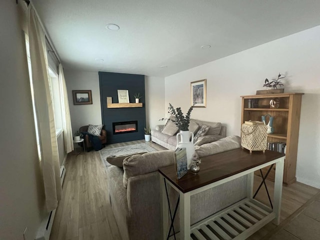 living room featuring baseboard heating, wood finished floors, and a glass covered fireplace