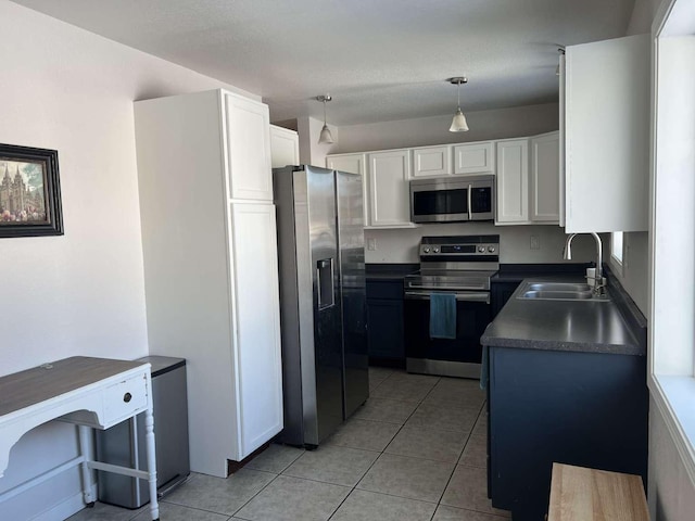 kitchen featuring light tile patterned floors, stainless steel appliances, a sink, white cabinets, and dark countertops