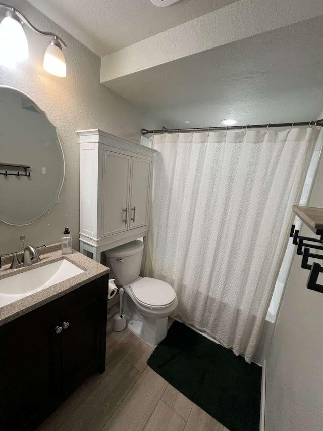 bathroom featuring a textured wall, toilet, vanity, a textured ceiling, and wood finished floors