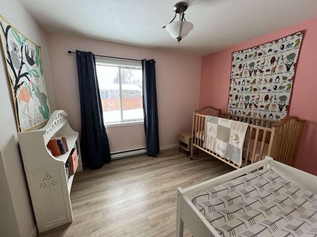 bedroom featuring a textured ceiling, a baseboard heating unit, baseboards, light wood-style floors, and a nursery area