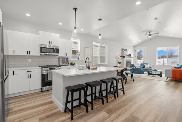 kitchen with a breakfast bar area, stainless steel appliances, light wood-style floors, a glass covered fireplace, and open floor plan