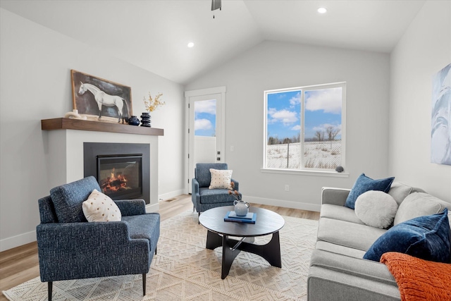 living area featuring vaulted ceiling, light wood finished floors, a glass covered fireplace, and baseboards