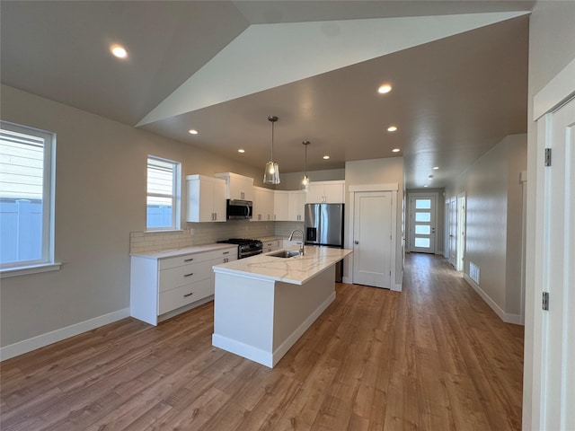 kitchen featuring appliances with stainless steel finishes, light wood-style floors, white cabinetry, a sink, and an island with sink