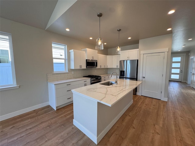 kitchen with stainless steel appliances, wood finished floors, a sink, decorative backsplash, and a center island with sink