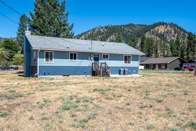 rear view of property featuring a mountain view, a lawn, roof with shingles, crawl space, and a chimney