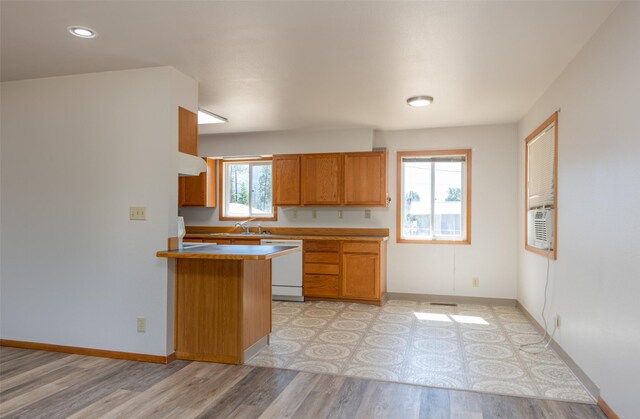 kitchen featuring range hood, brown cabinets, white dishwasher, a sink, and light wood-type flooring