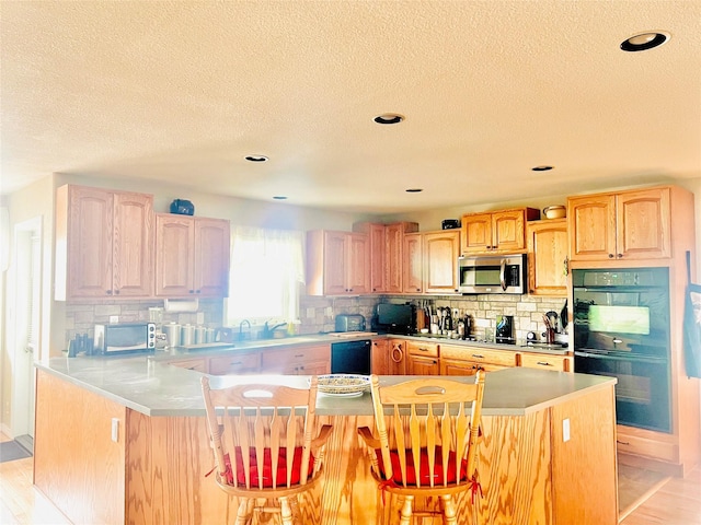 kitchen featuring tasteful backsplash, stainless steel microwave, a breakfast bar area, and dobule oven black