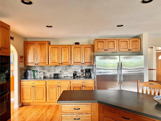 kitchen featuring backsplash, black oven, arched walkways, freestanding refrigerator, and brown cabinetry