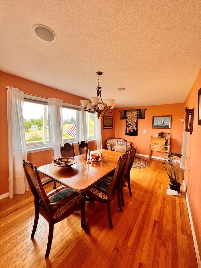 dining area with an inviting chandelier, light wood-style floors, baseboards, and a textured ceiling