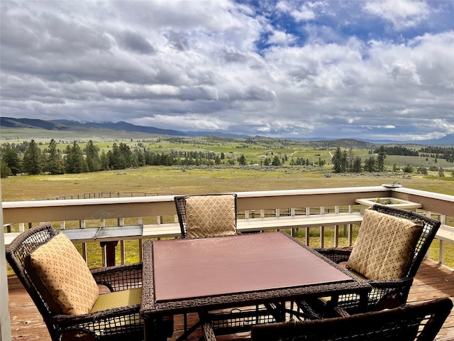 wooden deck featuring outdoor dining area, a mountain view, and a rural view