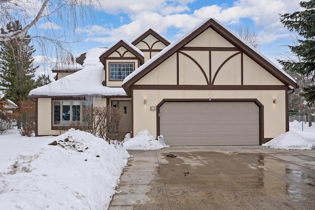 english style home featuring a garage, driveway, fence, and stucco siding