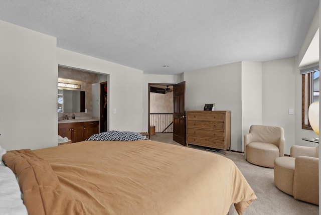 bedroom with light carpet, ensuite bath, a textured ceiling, and a sink