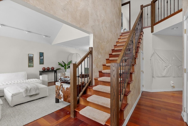 stairs featuring baseboards, a high ceiling, track lighting, and wood finished floors