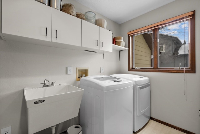 clothes washing area featuring a sink, baseboards, washer and dryer, cabinet space, and light floors