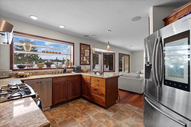 kitchen with brown cabinets, stainless steel appliances, open floor plan, a sink, and light stone countertops