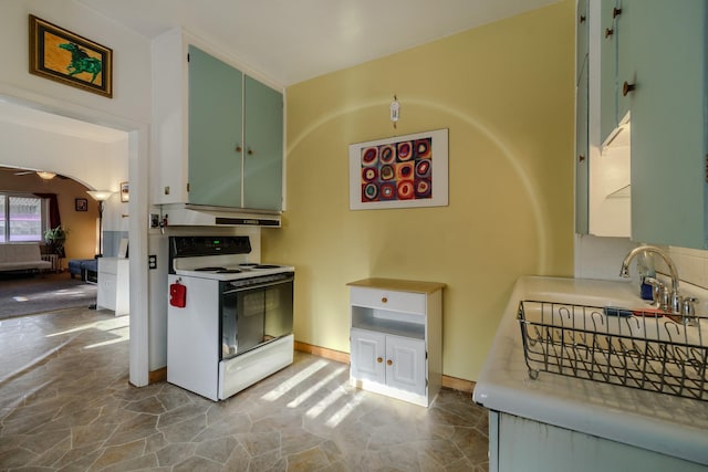 kitchen featuring arched walkways, electric range oven, stone finish floor, a sink, and baseboards