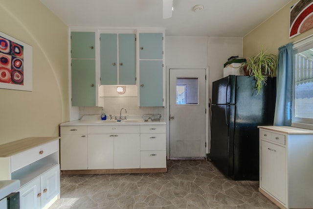 kitchen featuring a sink, light countertops, backsplash, a wealth of natural light, and freestanding refrigerator