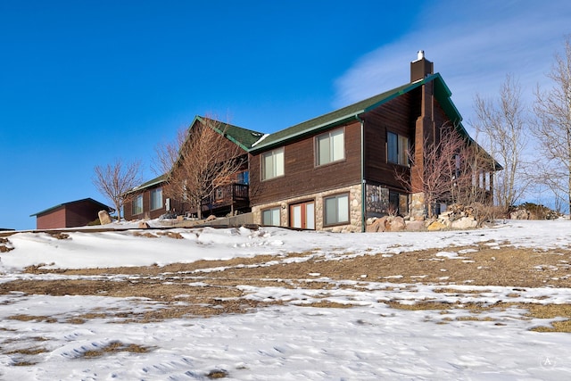 view of snow covered exterior featuring stone siding, a chimney, and an attached garage