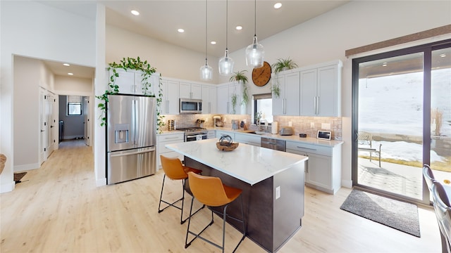 kitchen featuring stainless steel appliances, a high ceiling, light wood-style floors, a center island, and decorative light fixtures