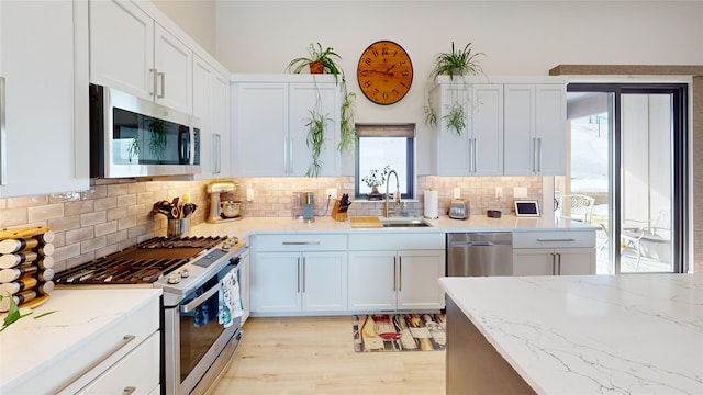 kitchen with light stone counters, a sink, appliances with stainless steel finishes, decorative backsplash, and light wood finished floors