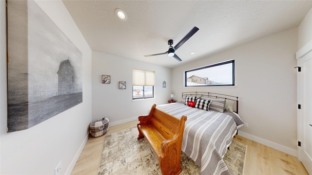 bedroom featuring ceiling fan, a textured ceiling, baseboards, and wood finished floors