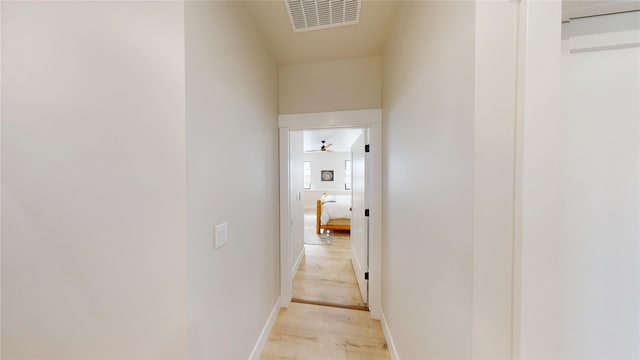 hallway featuring light wood-type flooring, baseboards, and visible vents