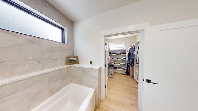 bathroom featuring wood finished floors, a bath, and a walk in closet