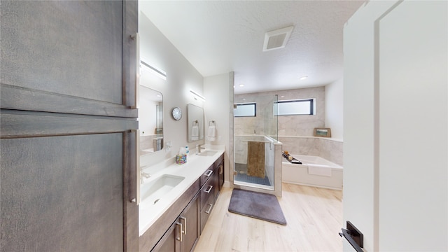 bathroom with a garden tub, double vanity, a sink, a shower stall, and wood finished floors