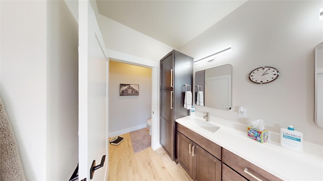 bathroom with toilet, wood finished floors, vanity, and baseboards