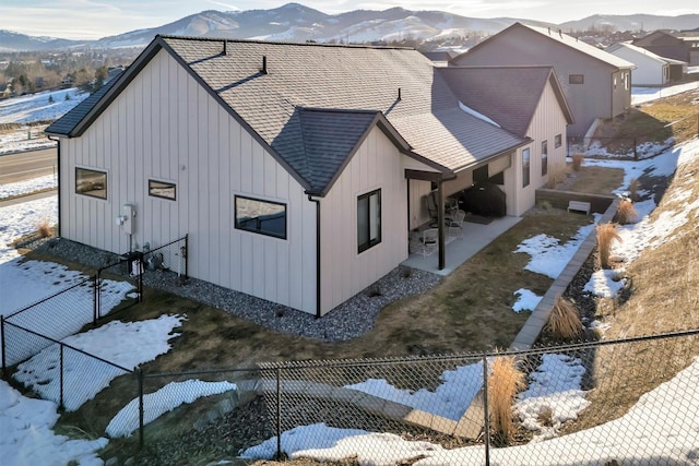 exterior space featuring a shingled roof, board and batten siding, a patio area, a mountain view, and a fenced backyard