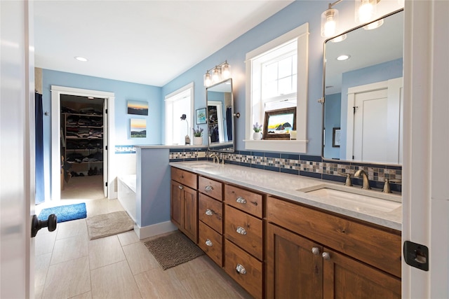 full bath with double vanity, backsplash, a sink, and a walk in closet