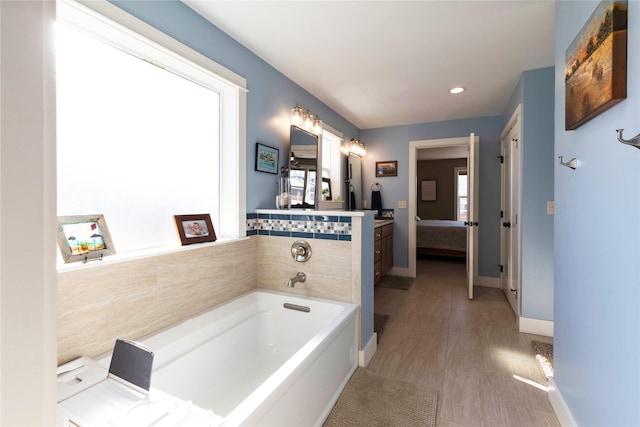 ensuite bathroom with a healthy amount of sunlight, a garden tub, vanity, and ensuite bathroom