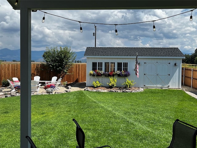 exterior space featuring a fenced backyard, a fire pit, an outdoor structure, roof with shingles, and a front yard