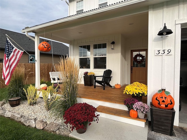 entrance to property featuring board and batten siding, covered porch, and fence