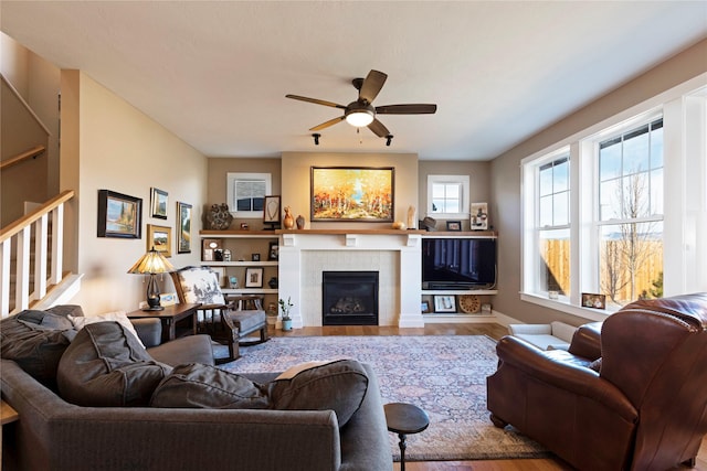 living room with stairs, wood finished floors, a tile fireplace, and a ceiling fan