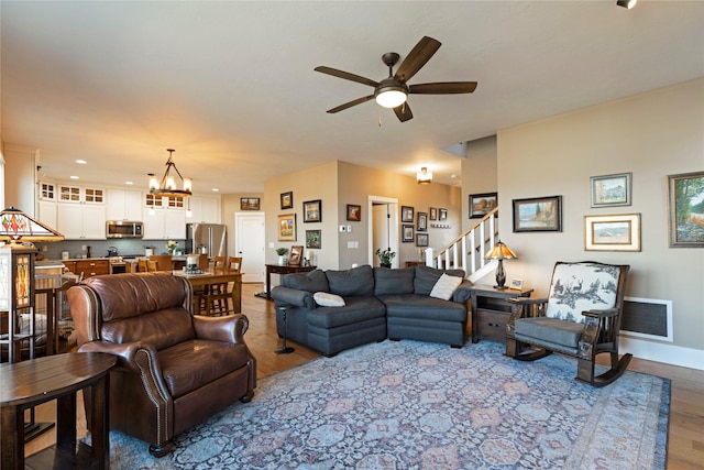 living area with ceiling fan with notable chandelier, visible vents, baseboards, and wood finished floors