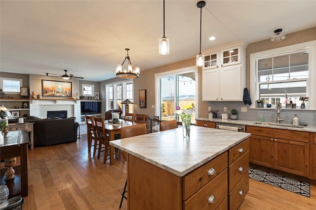 kitchen featuring a fireplace, light wood-style flooring, decorative backsplash, a kitchen island, and a sink