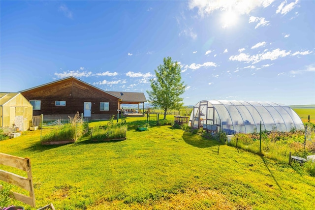 view of yard featuring a greenhouse, a vegetable garden, an outdoor structure, and fence