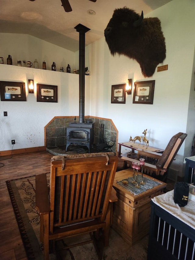 interior space with baseboards, a ceiling fan, lofted ceiling, wood finished floors, and a wood stove