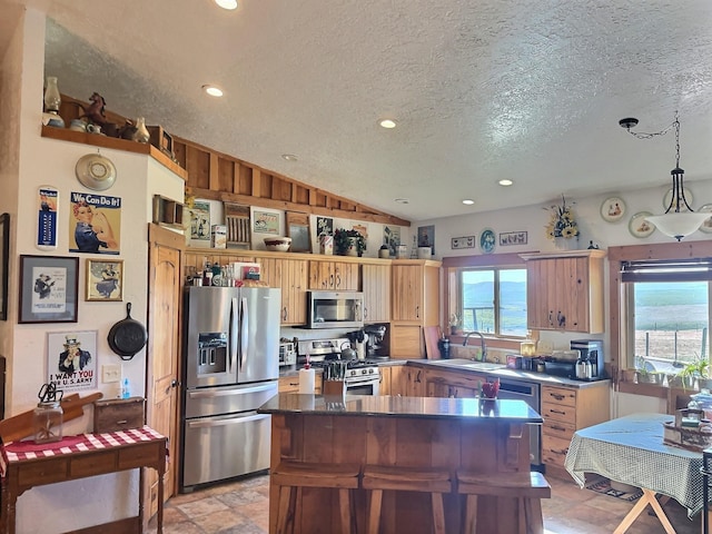 kitchen with a textured ceiling, a kitchen island, a sink, vaulted ceiling, and appliances with stainless steel finishes