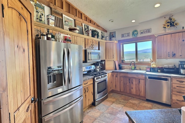 kitchen with recessed lighting, appliances with stainless steel finishes, vaulted ceiling, a sink, and a textured ceiling