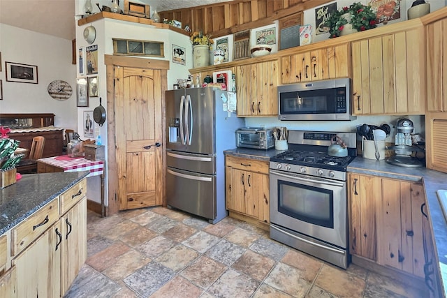 kitchen featuring a toaster, dark stone counters, stone finish flooring, and stainless steel appliances