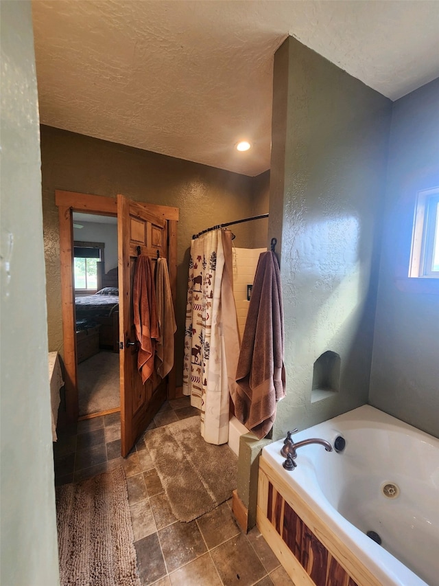 ensuite bathroom with ensuite bathroom, stone finish flooring, a shower with shower curtain, a tub with jets, and a textured wall