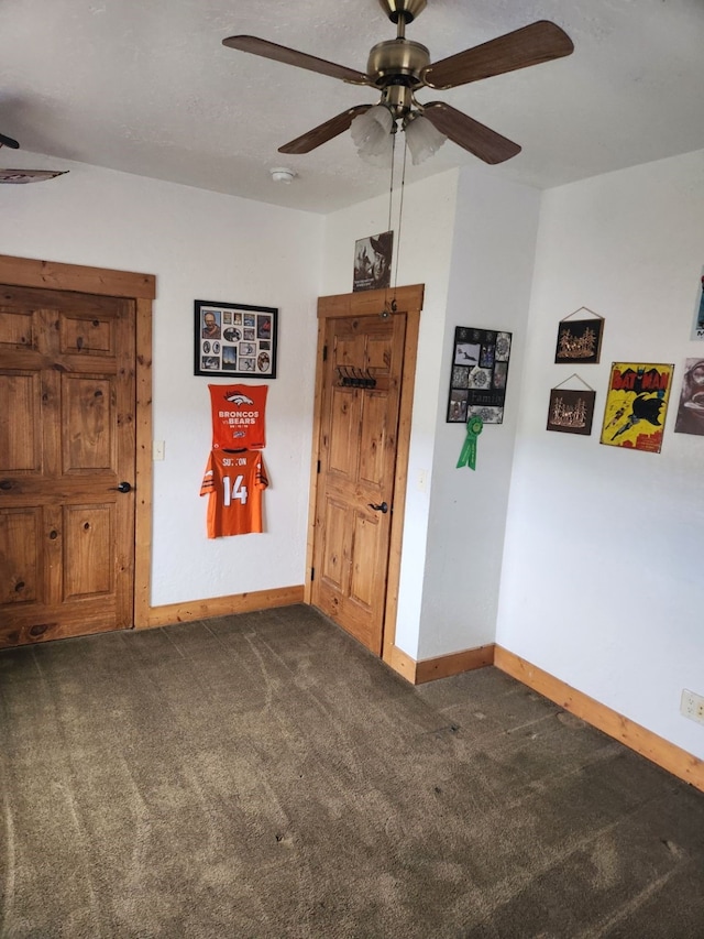 unfurnished room with a ceiling fan, dark colored carpet, and baseboards