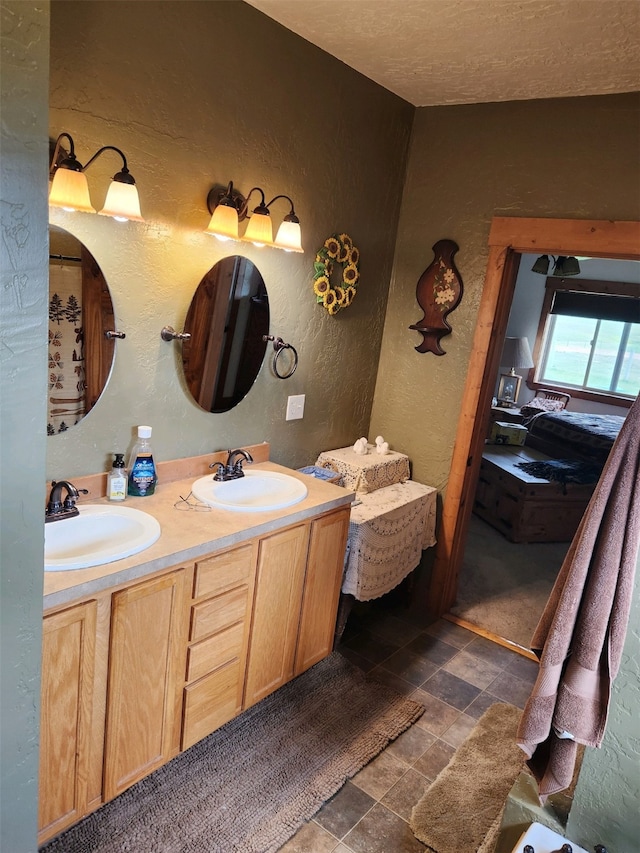 bathroom featuring double vanity, stone finish floor, a textured wall, and a sink