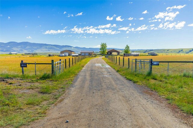 view of street with a rural view, a mountain view, and dirt driveway